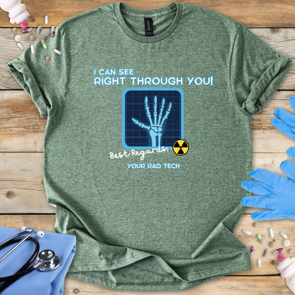 Heather military green t-shirt with medical-radiology themed graphic and 'I can see right through you' text on a wooden surface with medical gloves.