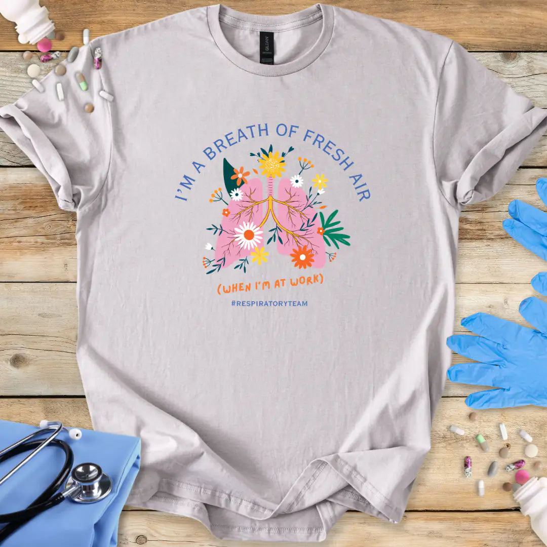 Ice-Gray med t-shirt with a colorful respiratory therapy graphic and 'I'm a breath of fresh air' text on a wooden surface with medical supplies.
