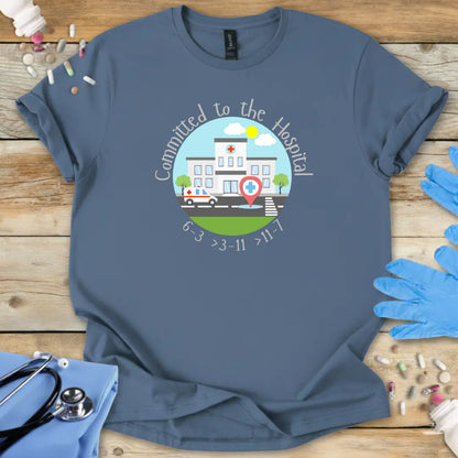 Indigo blue t-shirt with a hospital-themed graphic and 'Committed To The Hospital' on a wooden surface with medical supplies.