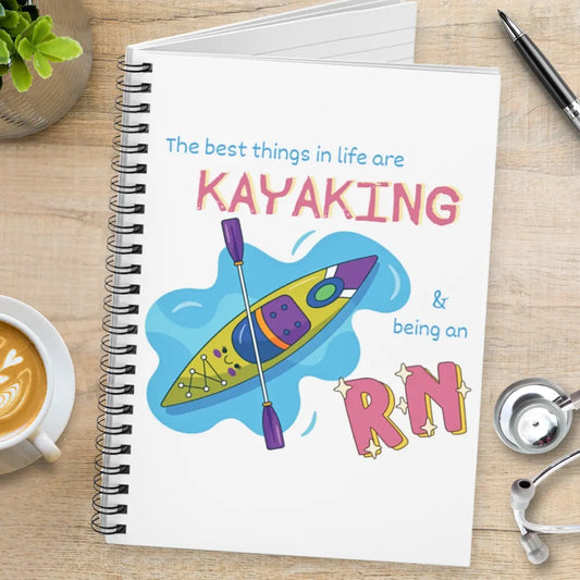 Medical spiral notebook with kayaking and RN illustration on a wooden surface with coffee and stethoscope.