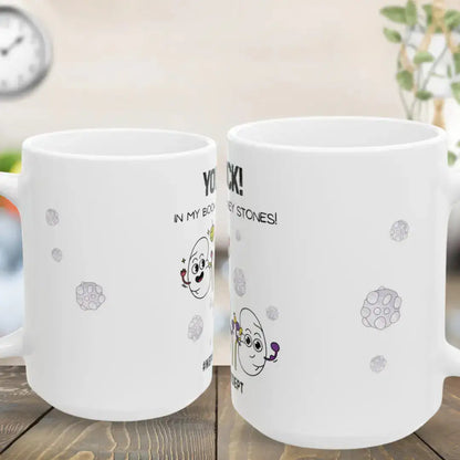 Two white mugs with cartoon designs and text on a wooden surface.
