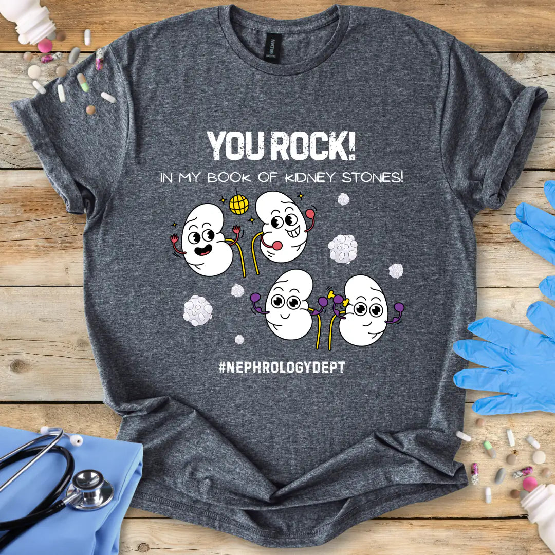 Dark Heather Grey t-shirt with cartoon kidneys and 'You rock in my book of kidney stones, nephrology dept.' text on a wooden surface with medical accessories.