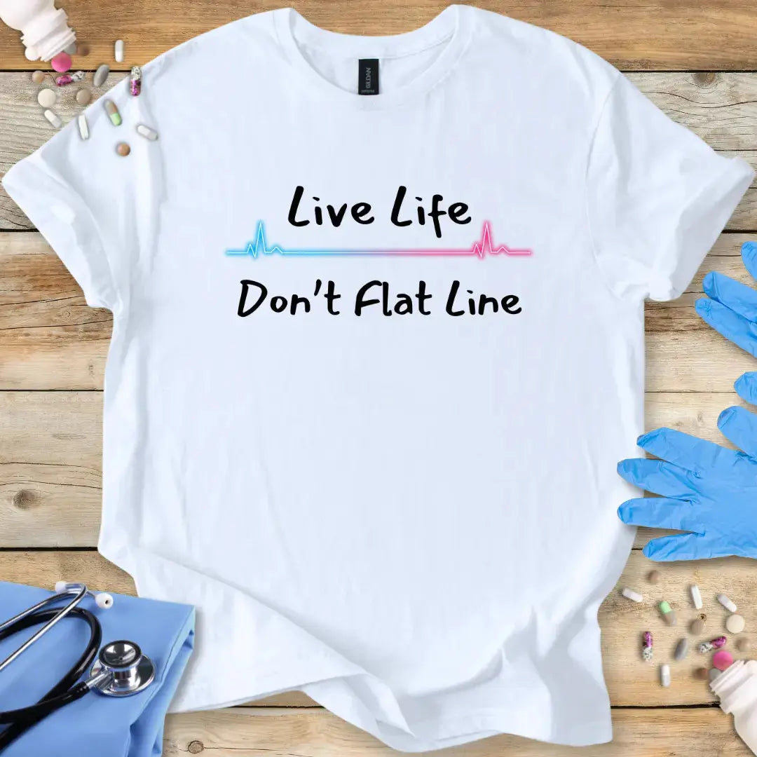 White t-shirt with 'Live Life Don't Flat Line' text on a wooden surface with medical items.