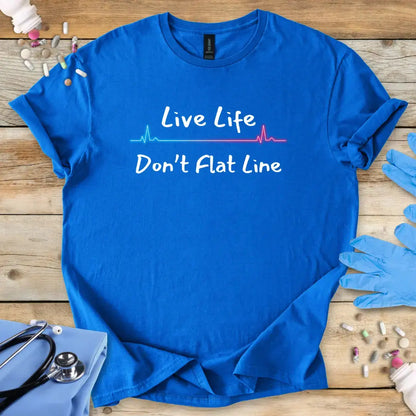 Blue med t-shirt with 'Live Life Don't Flat Line' text on a wooden surface with medical items.