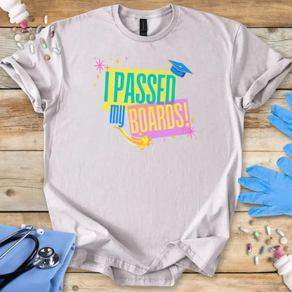 Gray t-shirt with 'I Passed My Boards!' text on a wooden surface with medical supplies.