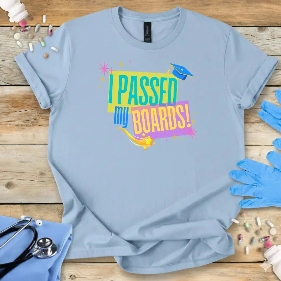 Light blue t-shirt with 'I Passed My Boards!' design on a wooden surface with medical items.