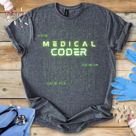 Gray t-shirt with 'Medical Coder' text on a wooden surface with medical items.