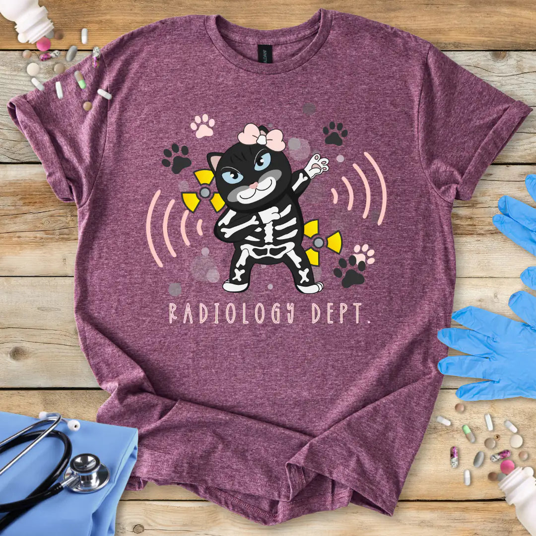 Heather Maroon t-shirt with a cartoon cat skeleton design labeled 'Radiology Dept.' on a wooden surface with medical-themed items.