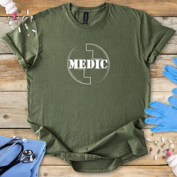 Military green t-shirt with 'MEDIC' logo on a wooden surface with medical accessories.