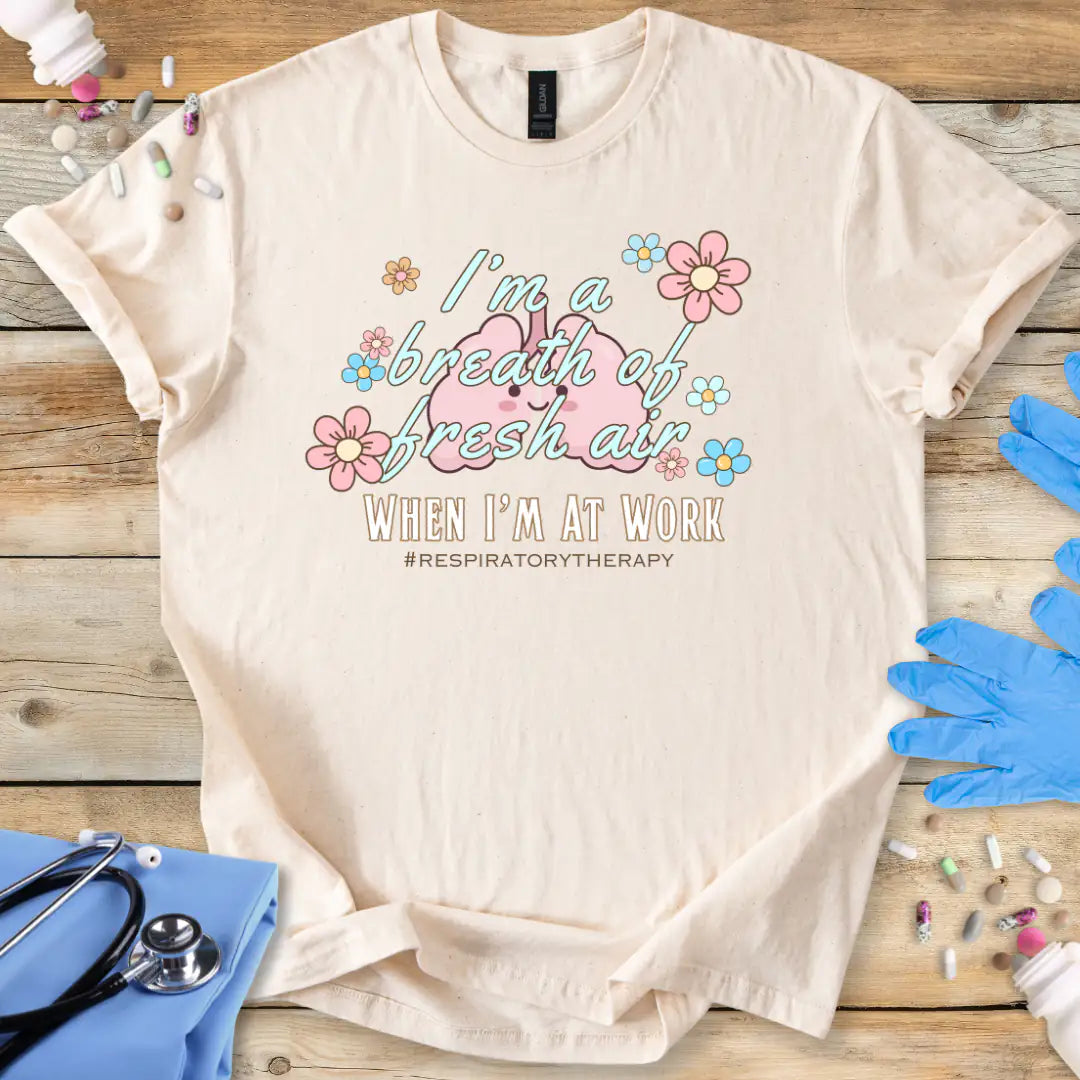  Natural t-shirt with lung cartoon character and 'I'm a breath of fresh air when I'm at work' text on a wooden surface with medical supplies.