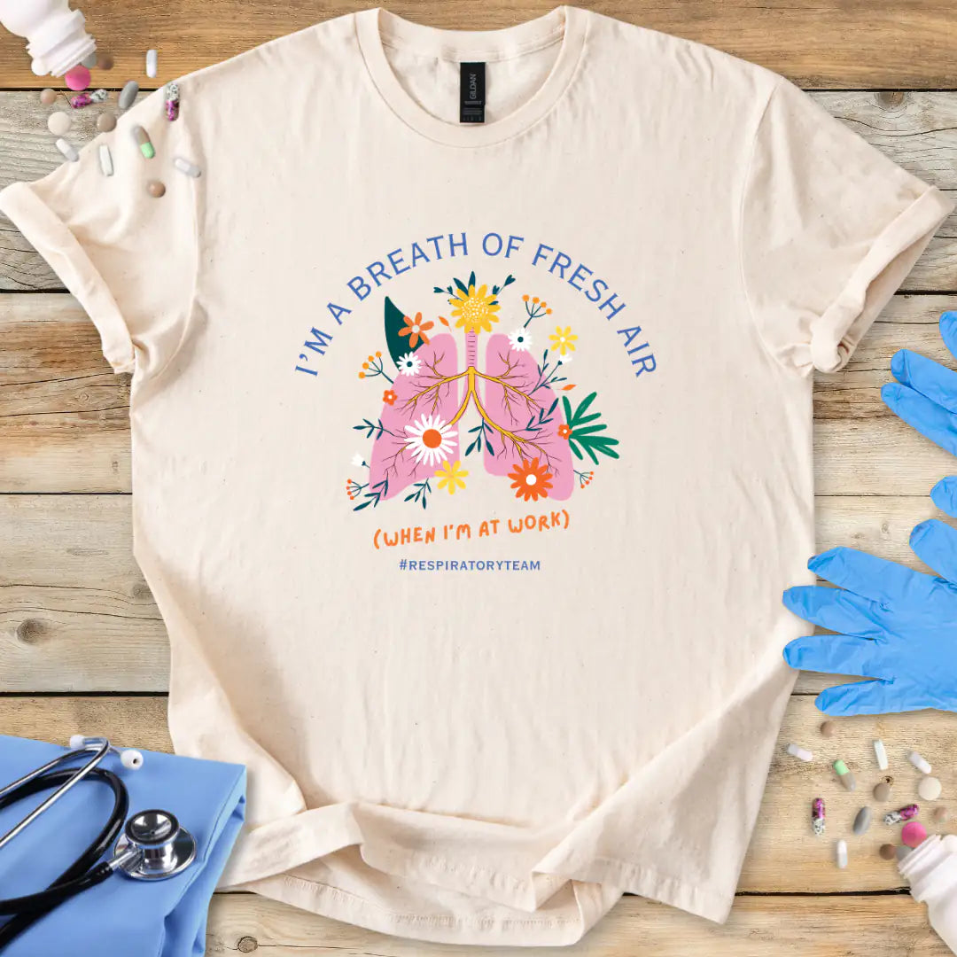 Natural med t-shirt with a colorful respiratory therapy graphic and 'I'm a breath of fresh air' text on a wooden surface with medical supplies.