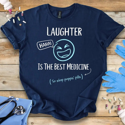 Navy blue t-shirt with medical humor text 'Laughter Is The Best Medicine' and graphics on a wooden surface with medical-themed items.