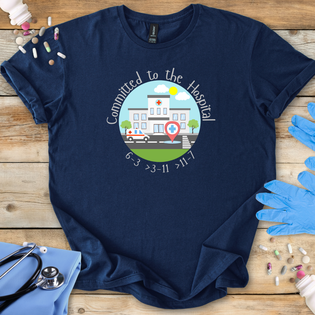 Navy med t-shirt with a hospital-themed graphic and 'Committed To The Hospital' on a wooden surface with medical supplies.