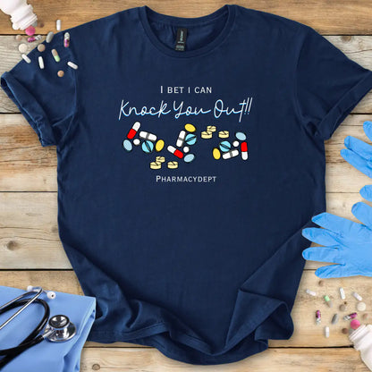 Navy med t-shirt with pharmacy-themed design with the text 'I bet i can knock you out' on a wooden surface with medical accessories.