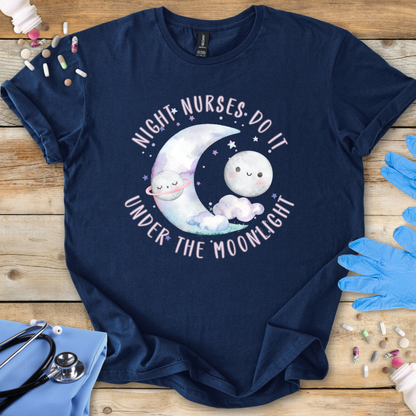 Navy blue t-shirt with cartoon design and 'Night Nurses Do It Under The Moonlight' text on a wooden surface with medical accessories.