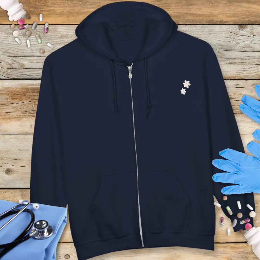 Navy zip-up hoodie front with two small white daisy icons on the chest, displayed flat on a wooden background with medical props.