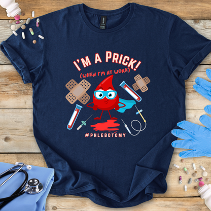 Navy t-shirt with a graphic design featuring a blood drop character and text 'I'm A Prick Phlebotomy' on a wooden surface with medical accessories.