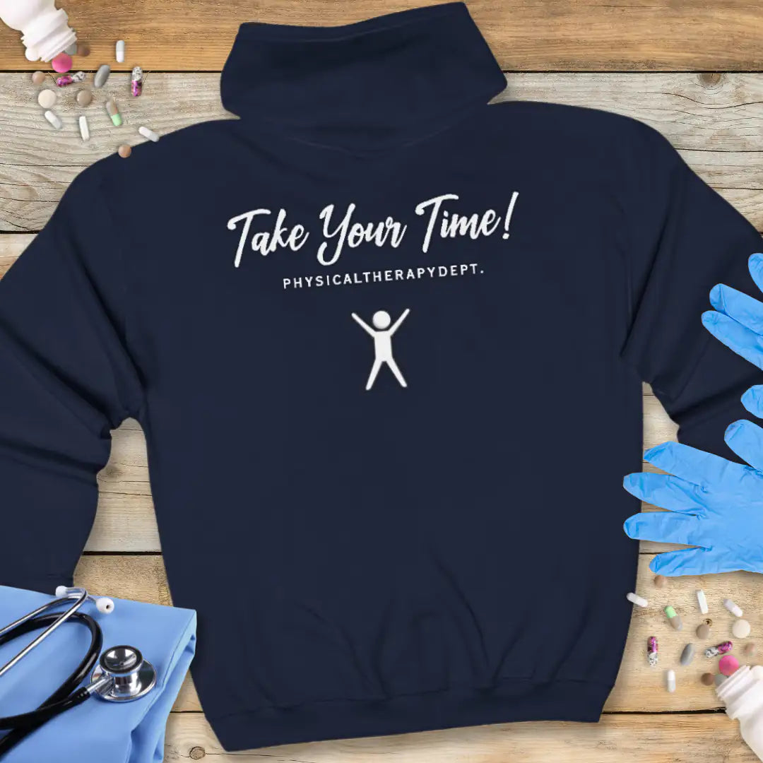 Navy hoodie back with 'Take Your Time! Physical Therapy Dept.' text and a white stick figure graphic, on a wooden background with medical props.