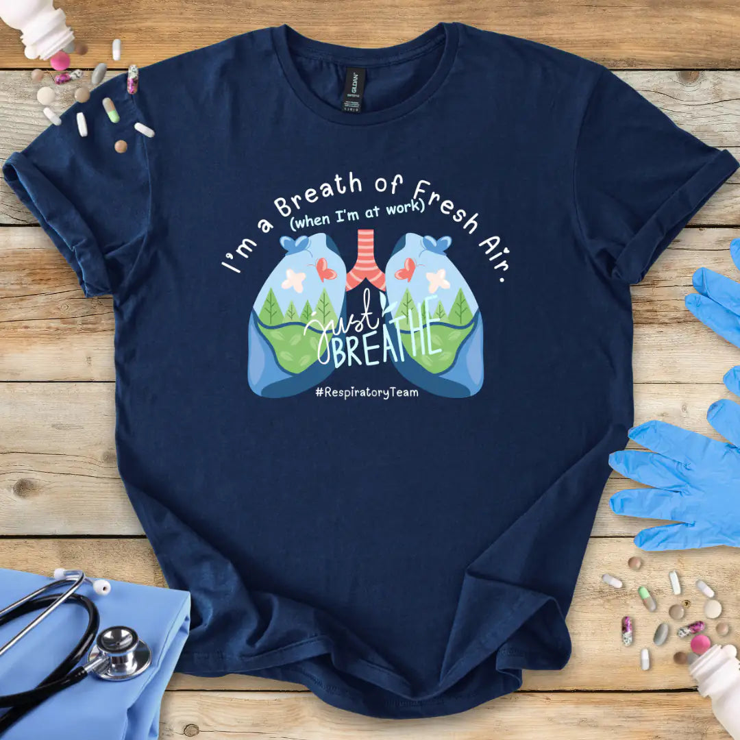 Navy blue t-shirt with respiratory therapy lungs design and text 'I'm a breath of Fresh Air' on a wooden surface with medical items.