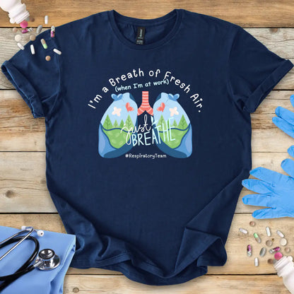 Navy blue t-shirt with respiratory therapy lungs design and text 'I'm a breath of Fresh Air' on a wooden surface with medical items.