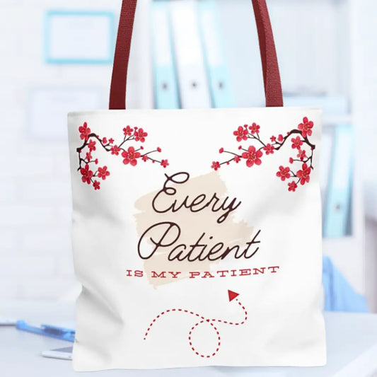 White canvas tote bag with dark red straps featuring 'Every Patient Is My Patient' in script, framed by red cherry blossom branch graphics and a dashed stethoscope loop design, on a blurred clinical background.