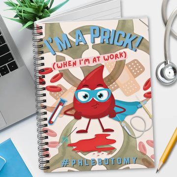 Notebook with a cartoon blood drop character and humorous phlebotomy text on a desk with medical-themed items.