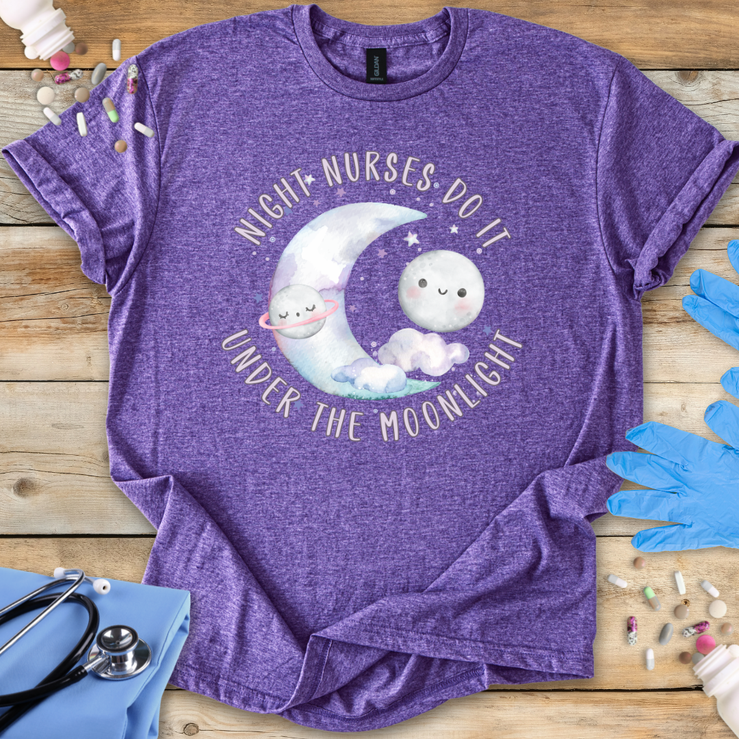 Purple t-shirt with a moon and cloud design and text 'Night nurses do it under the moonlight' on a wooden surface with medical supplies.