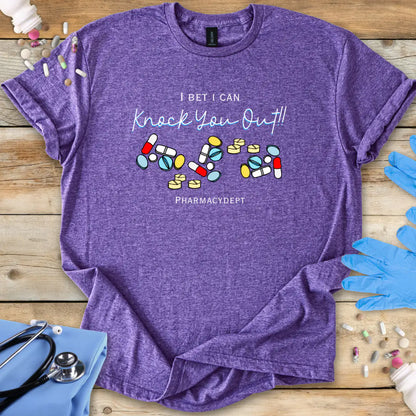 Heather purple t-shirt with pharmacy-themed design with the text 'I bet i can knock you out' on a wooden surface with medical accessories.