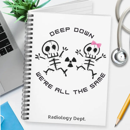 Notebook with skeleton design and 'Deep Down We're All The Same' text on a desk.