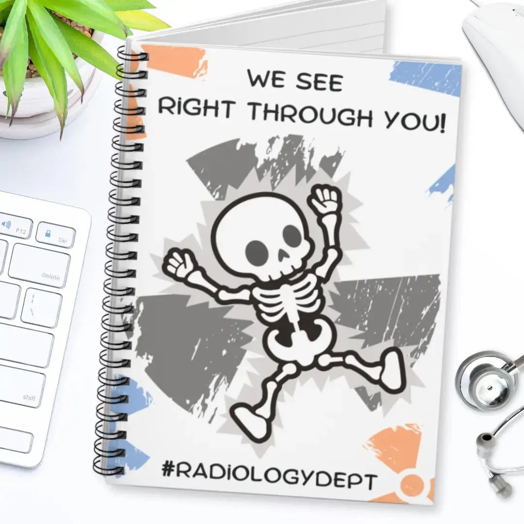 Radiology themed spiral notebook with skeleton design and text 'We see right through you! #radiologydept' on a desk with medical equipment.