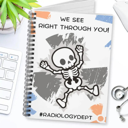 Radiology themed spiral notebook with skeleton design and text 'We see right through you! #radiologydept' on a desk with medical equipment.