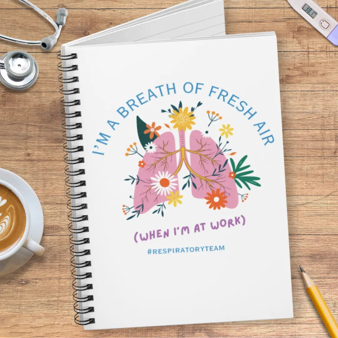 Notebook with a lungs illustration and 'I'm A Breath Of Fresh Air When I'm At Work' text on wooden surface with stethoscope.