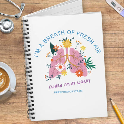 Notebook with a lungs illustration and 'I'm A Breath Of Fresh Air When I'm At Work' text on wooden surface with stethoscope.
