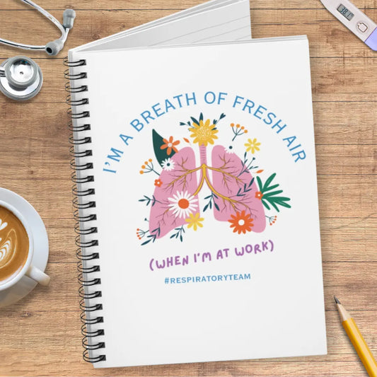 Notebook with a lungs illustration and 'I'm A Breath Of Fresh Air When I'm At Work' text on wooden surface with stethoscope.
