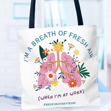 Tote bag with lungs and flowers design, text 'I'm a breath of fresh air (when I'm at work) #respiratoryteam' on a blurred medical background.