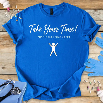 Blue t-shirt with 'Take Your Time! Physical Therapy Dept.' text and graphic on a wooden surface with medical items.