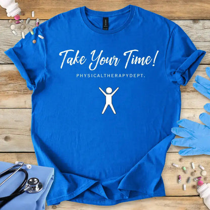 Blue t-shirt with 'Take Your Time! Physical Therapy Dept.' text and graphic on a wooden surface with medical items.