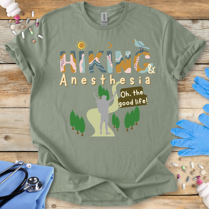 Green t-shirt with 'Hiking & Anesthesia Oh, the good life!' design on a wooden surface with medical supplies.