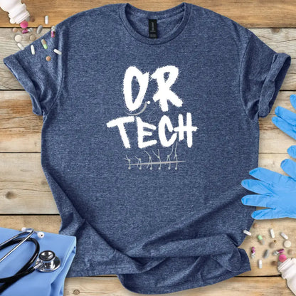 Blue t-shirt with 'O.R. TECH' text on a wooden surface with medical supplies.