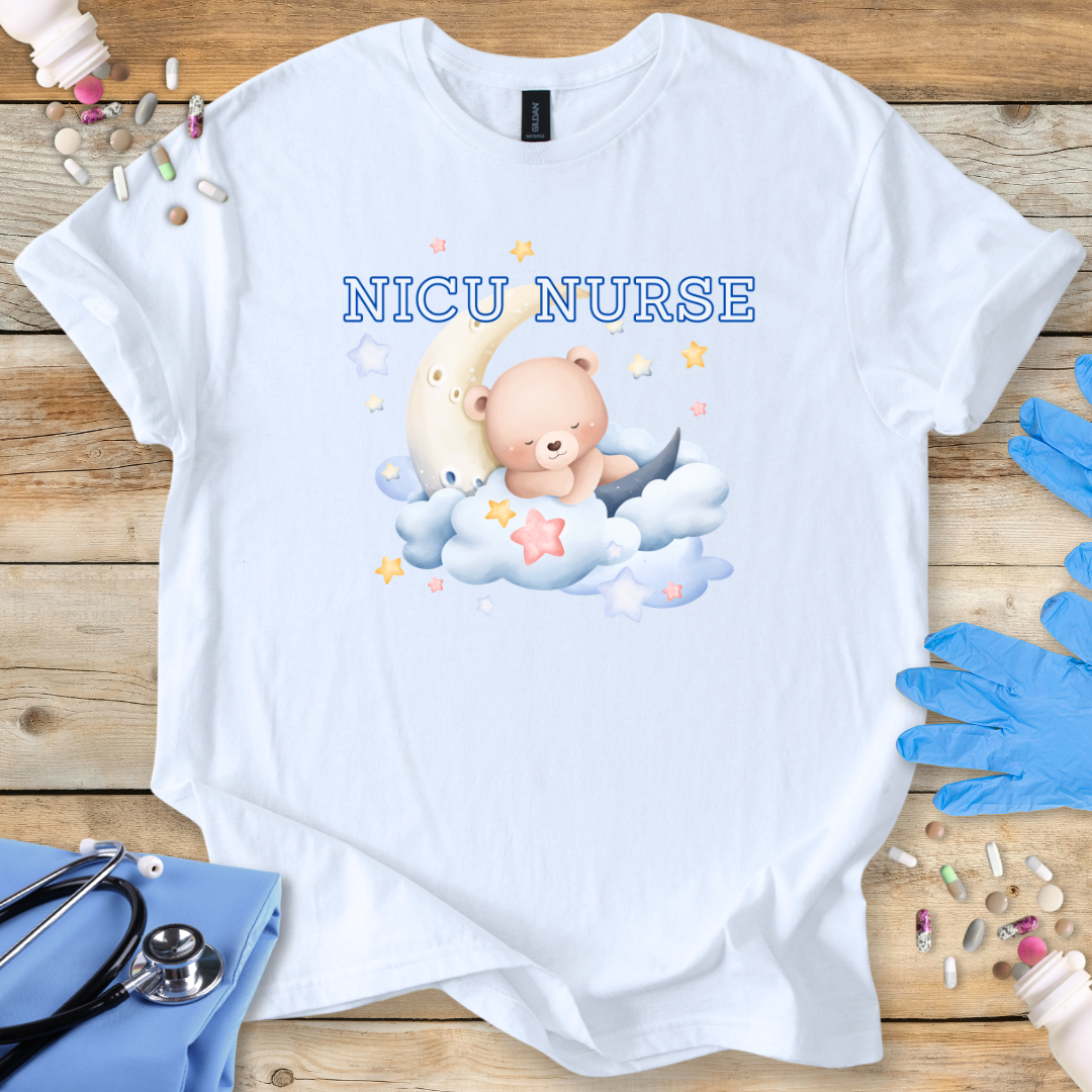 White t-shirt with NICU Nurse text  featuring a teddy bear and baby on a wooden surface with medical supplies.