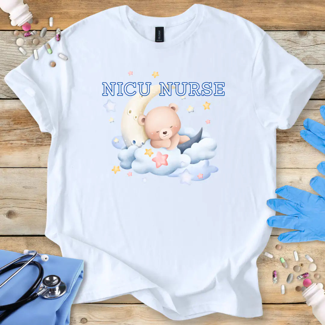 White t-shirt with NICU Nurse text  featuring a teddy bear and baby on a wooden surface with medical supplies.