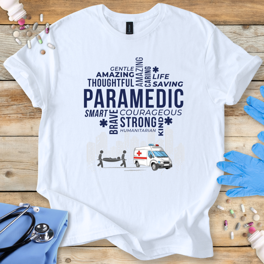 White t-shirt with paramedic-themed text and graphics on a wooden surface with medical accessories.